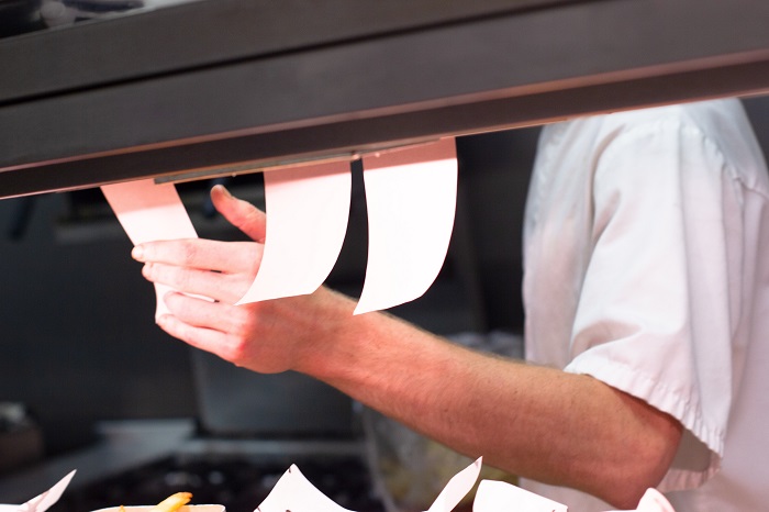 man's arm holding white paper tabs beneath kitchen pass