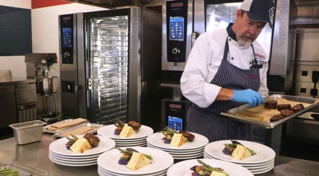 chef plating up food in restaurant kitchen with Rational combi ovens in background